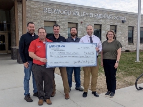 Group of people holding a check outside of the school. 