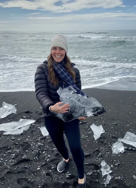 Hillary holding a chunk of ice next to the ocean.